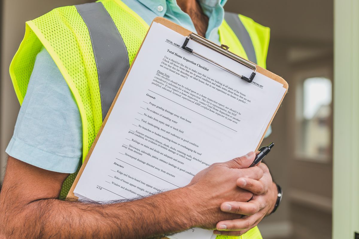 Close-up of an inspector in a high-visibility vest holding a clipboard with a printed home inspection checklist
